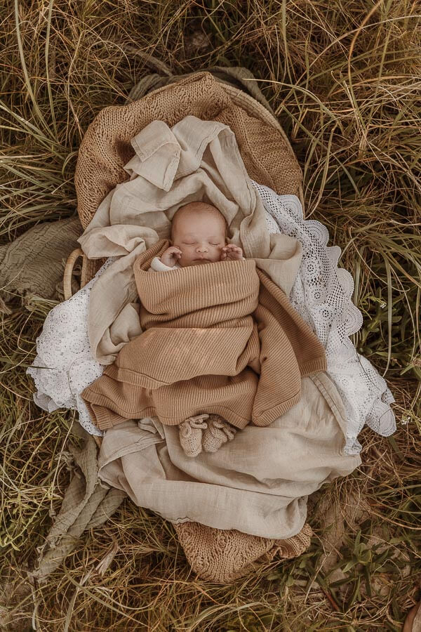 Newborn snuggled up in a nest of blankets at outdoor newborn session.