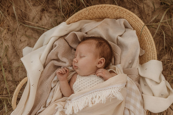 Newborn in basket amongst the sand dunes at photography session with Photos by Jordi.