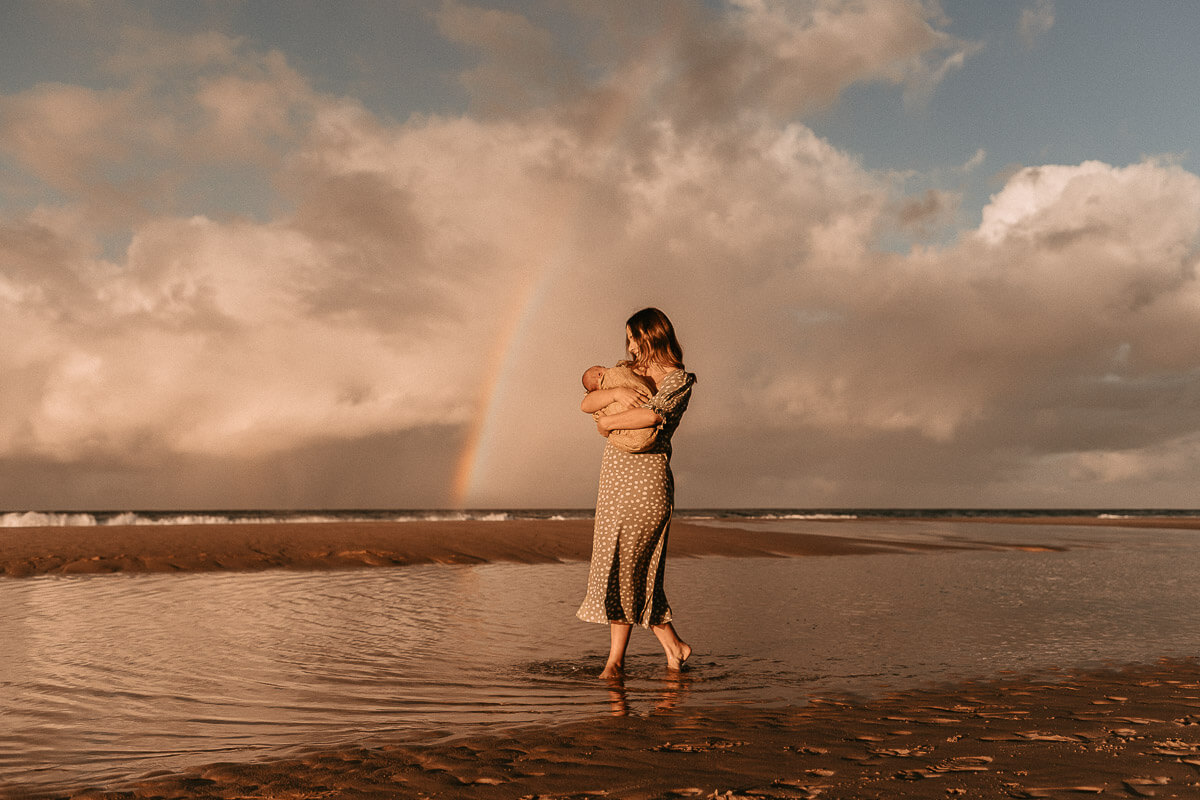 Mother and baby with rainbow backdrop at outdoor newborn photo session with Photos by Jordi.