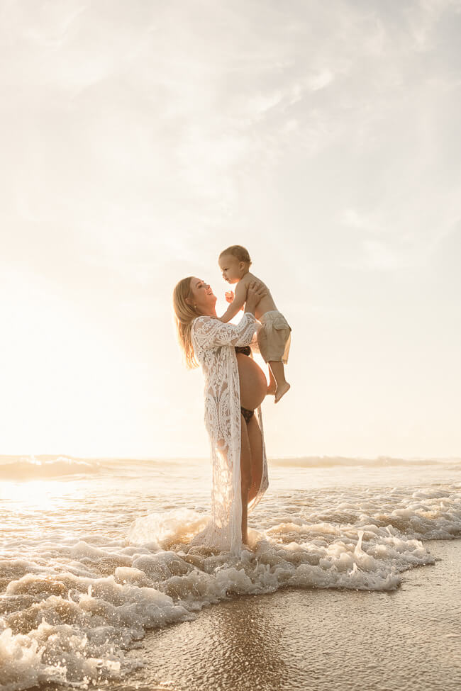A mother shares a sweet moment with her sons during a newborn photo session on the beach at sunrise.