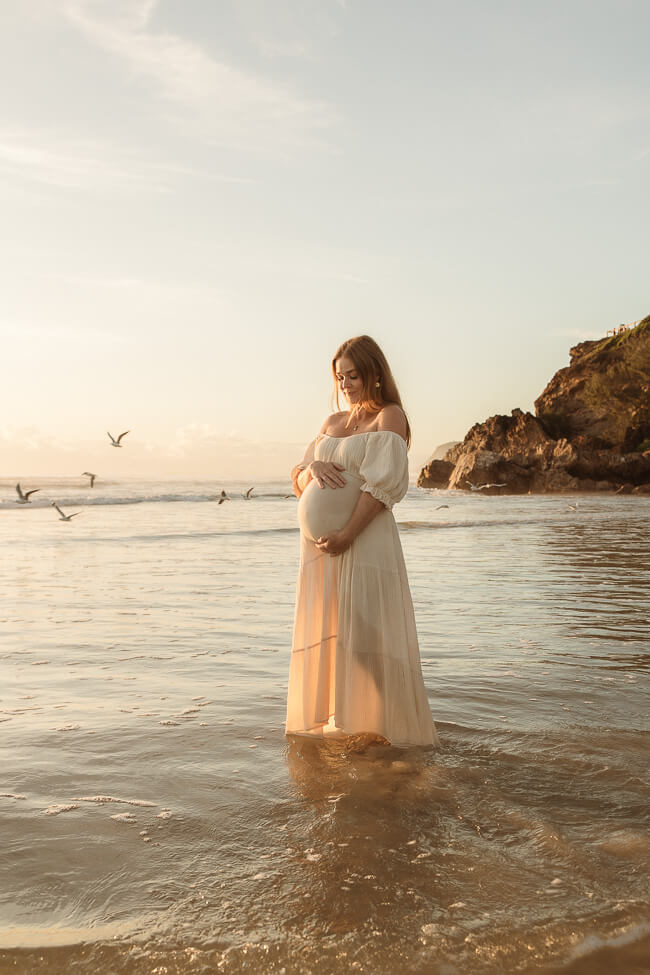 A mother shares a sweet moment with her sons during a newborn photo session on the beach at sunrise.