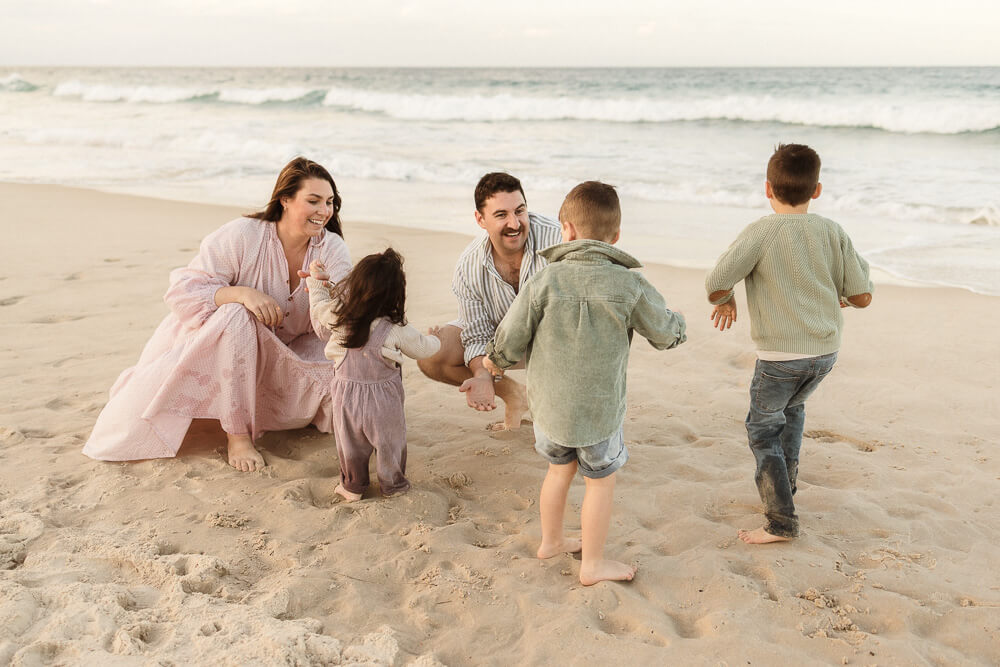 Winter-photoshoot-Gold-Coast-05 Family playing together on the beach during a winter photoshoot on the Gold Coast, with soft golden light and barefoot moments by the ocean.